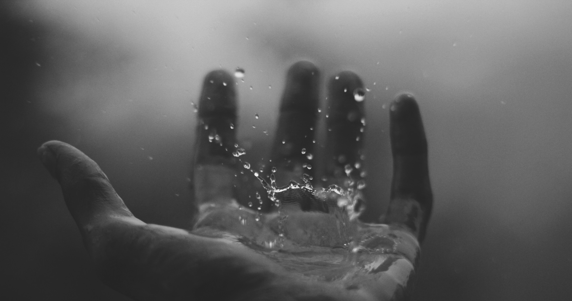 A hand breaking the surface of water, droplets suspended mid-splash against the palm.