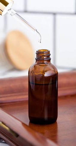 An amber glass dropper bottle with a glass pipette dropper, resting on a wooden surface.